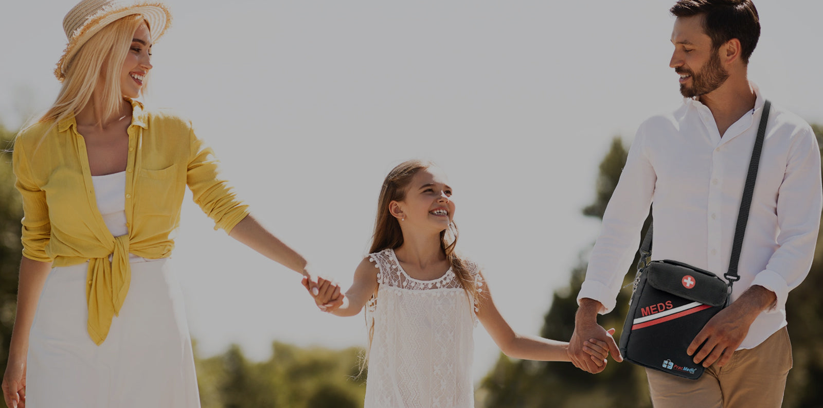 Smiling family walking outdoors, with the father carrying a PracMedic Bags black shoulder medicine bag labeled “MEDS,” designed for safe and convenient travel storage of emergency medications.